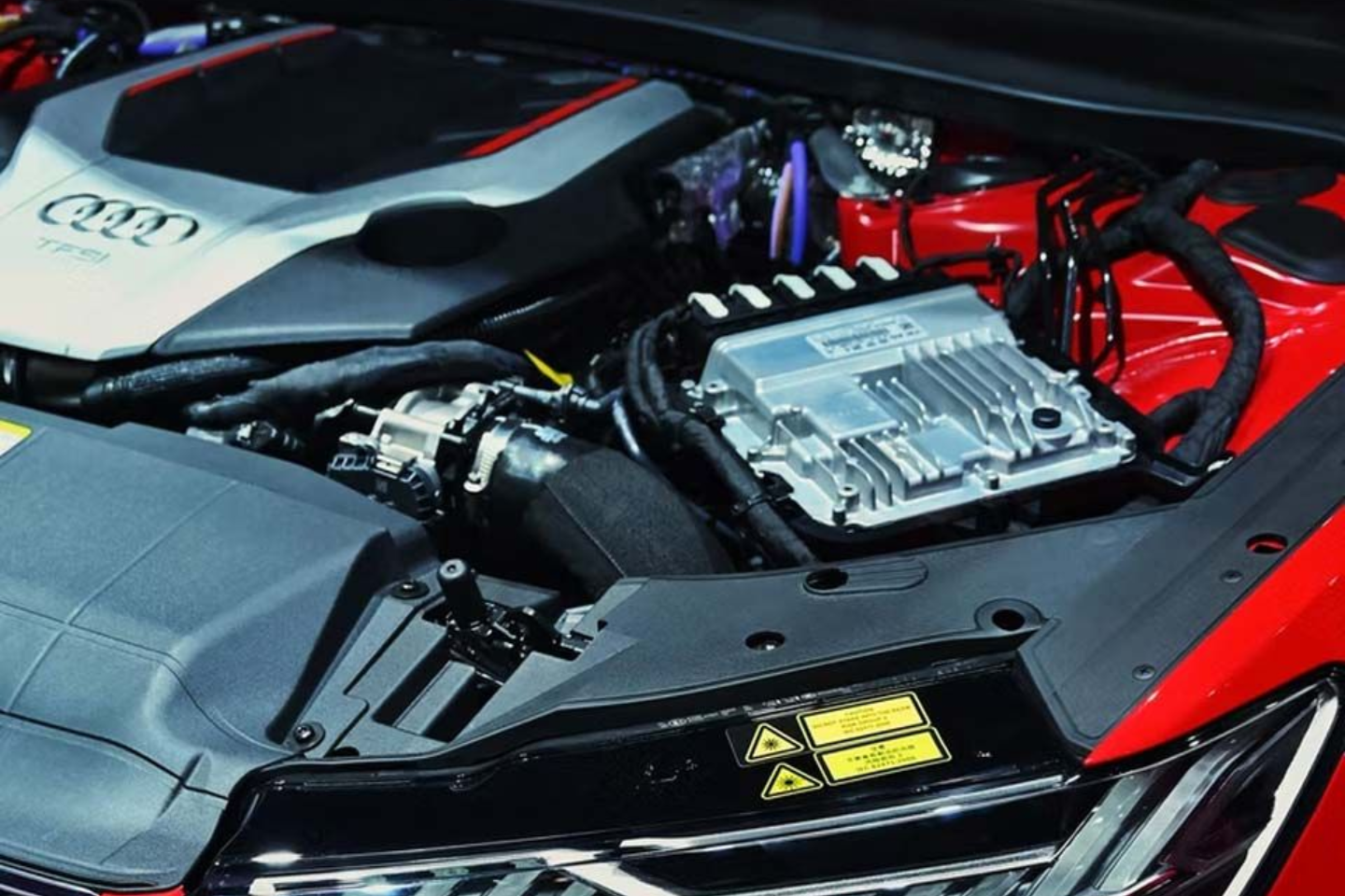 Audi car engine bay, featuring a gray engine cover and black components, including a silver module, on a red car.