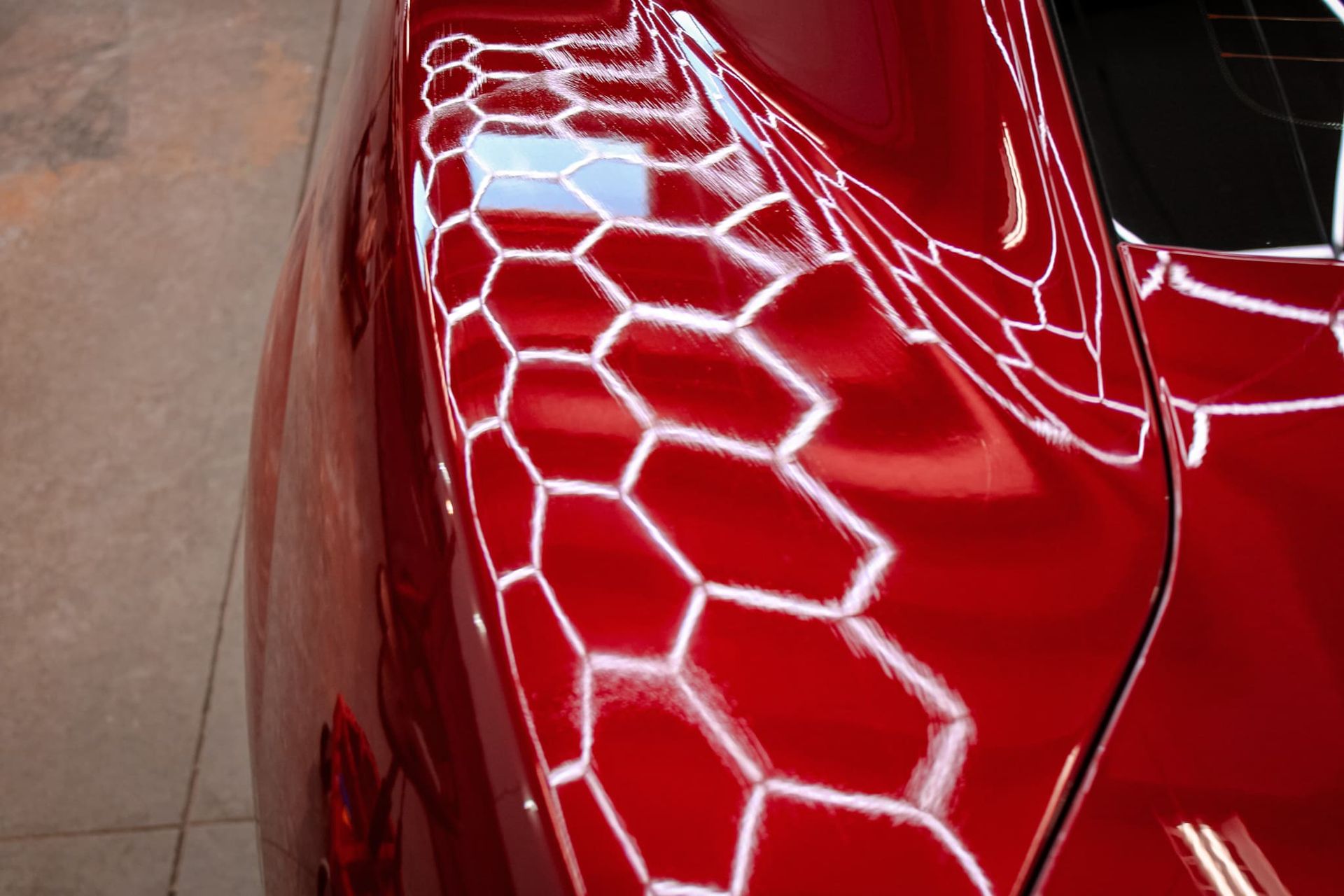 Red car body reflecting a honeycomb pattern of light.