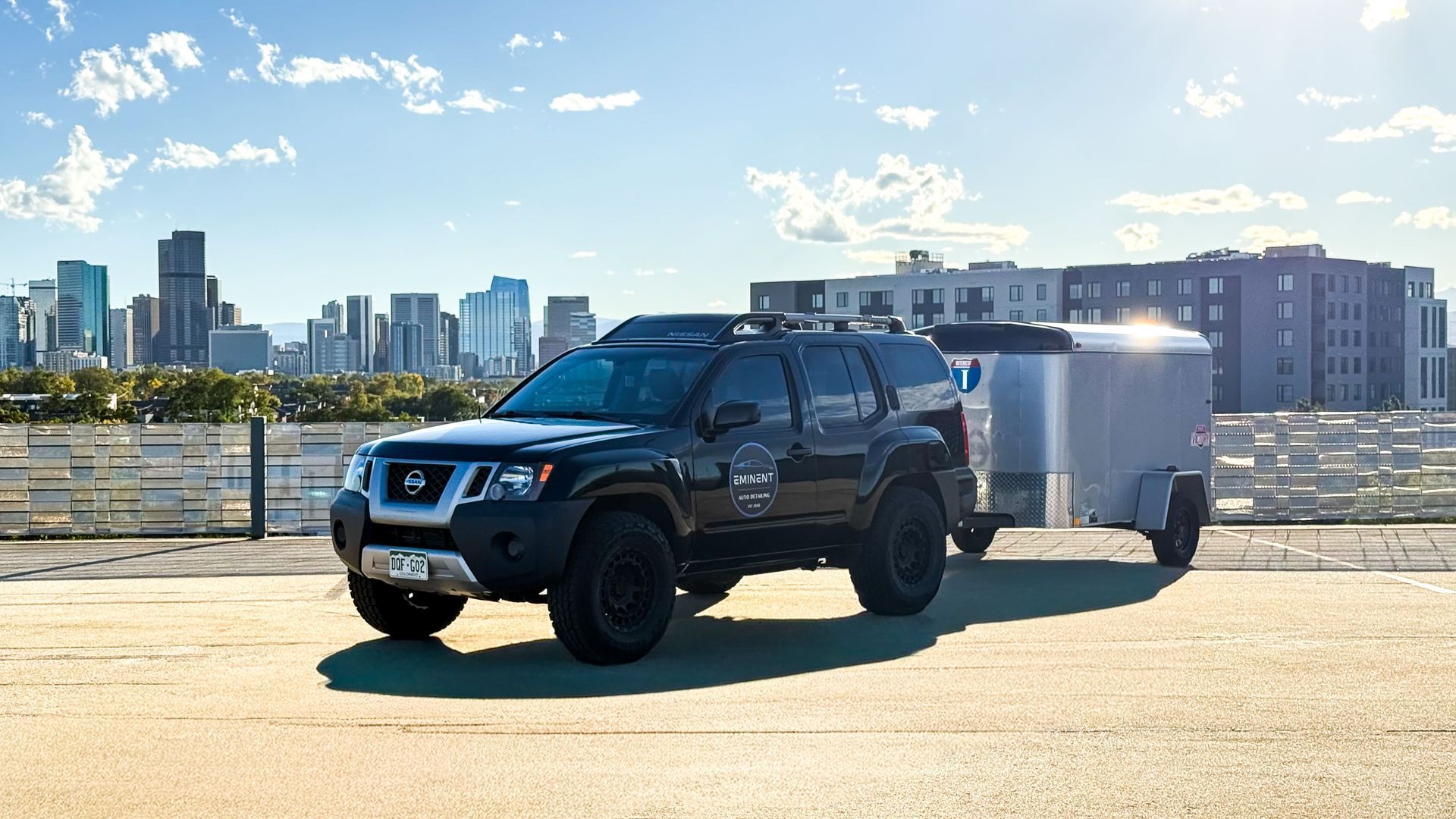 Black SUV towing a silver trailer in an urban setting with a skyline.