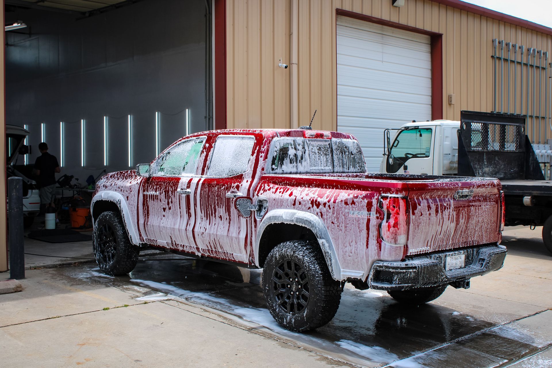 Red pickup truck covered in soap suds, outside a building, being washed.