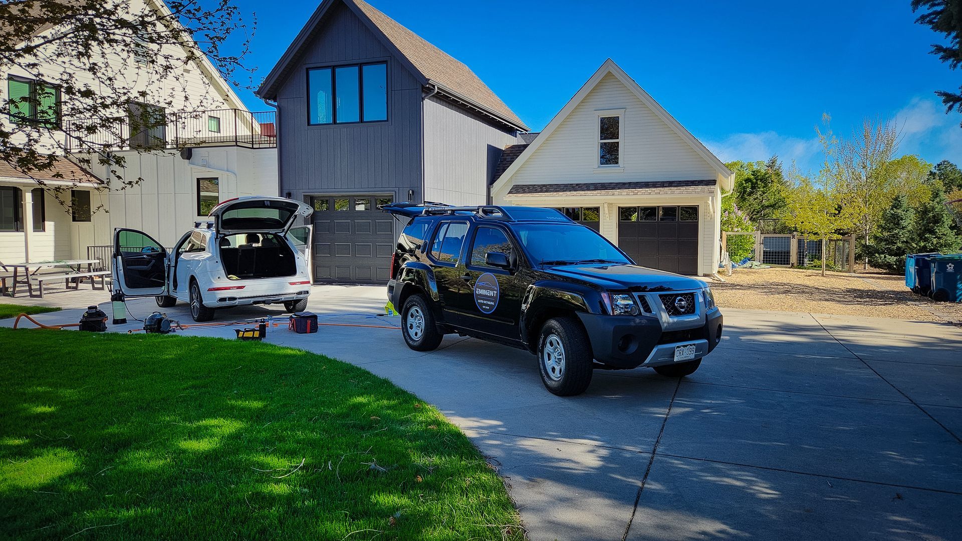 Black SUV parked in front of a house. White car with open doors beside it. Sunny day.