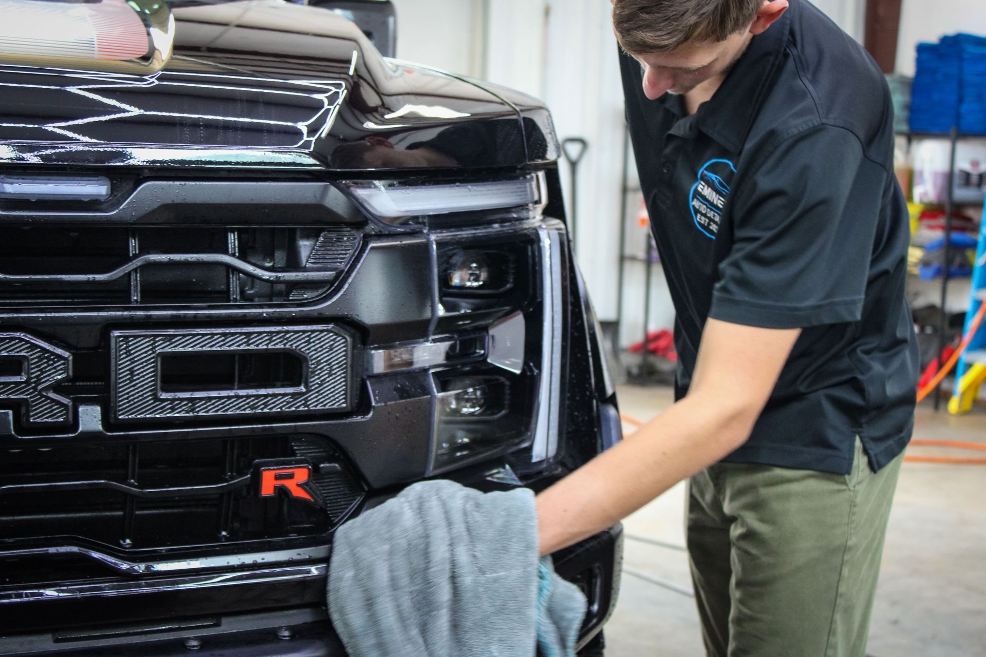 Person cleaning the front grill of a black truck with a gray cloth.