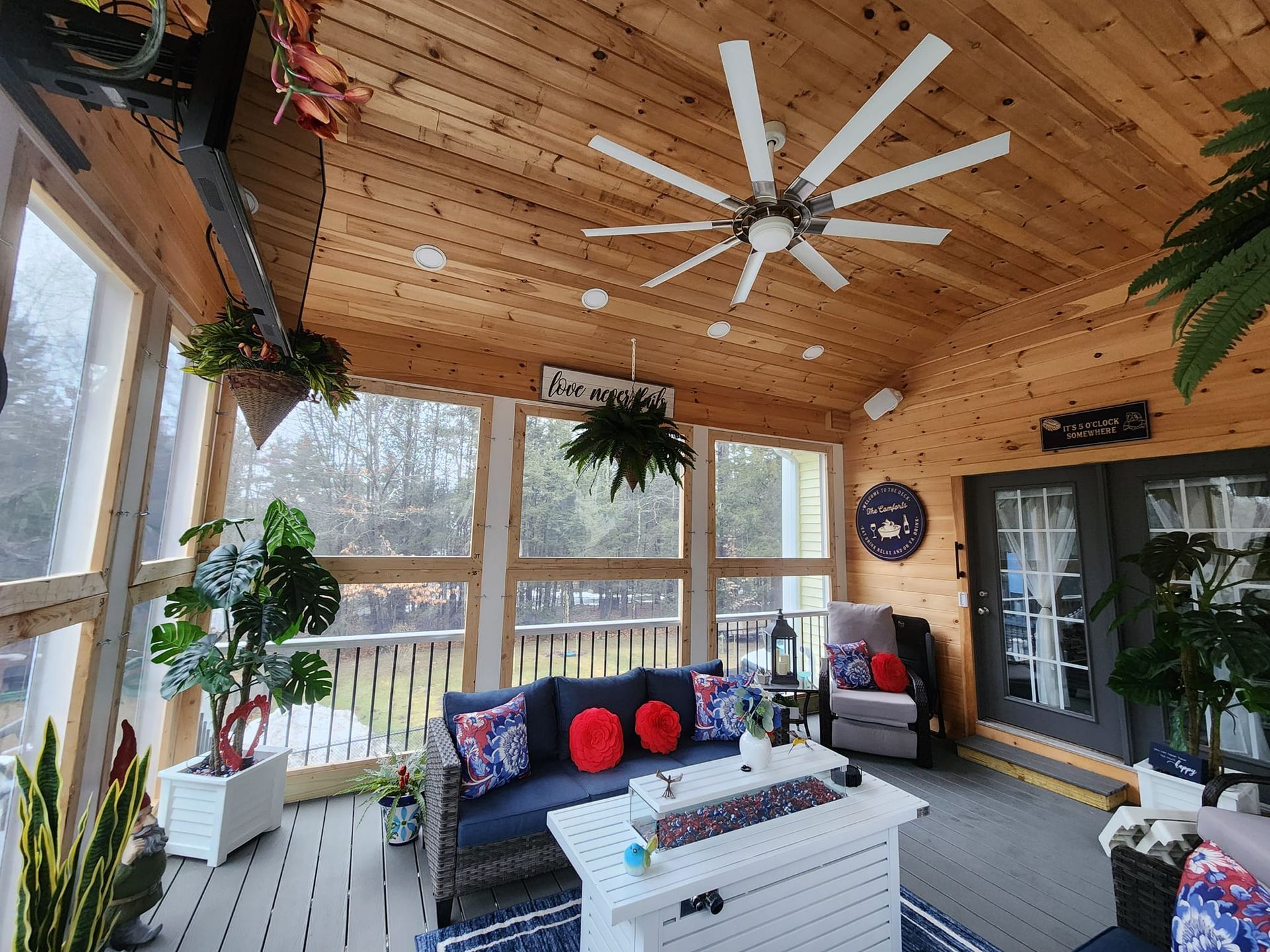 A screened in porch with a couch , chairs , and a ceiling fan.
