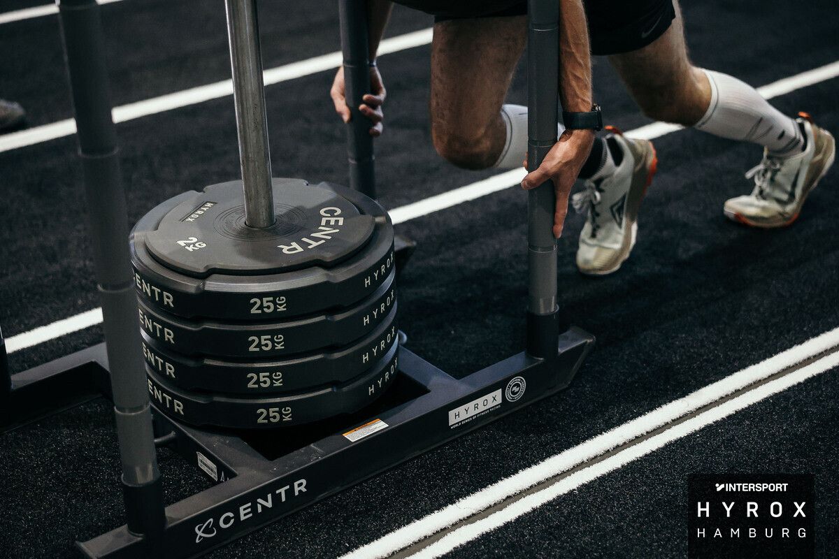 HYROX Sled Push Ein Mann schiebt einen Schlitten mit vier 25kg Scheiben beim HYROX