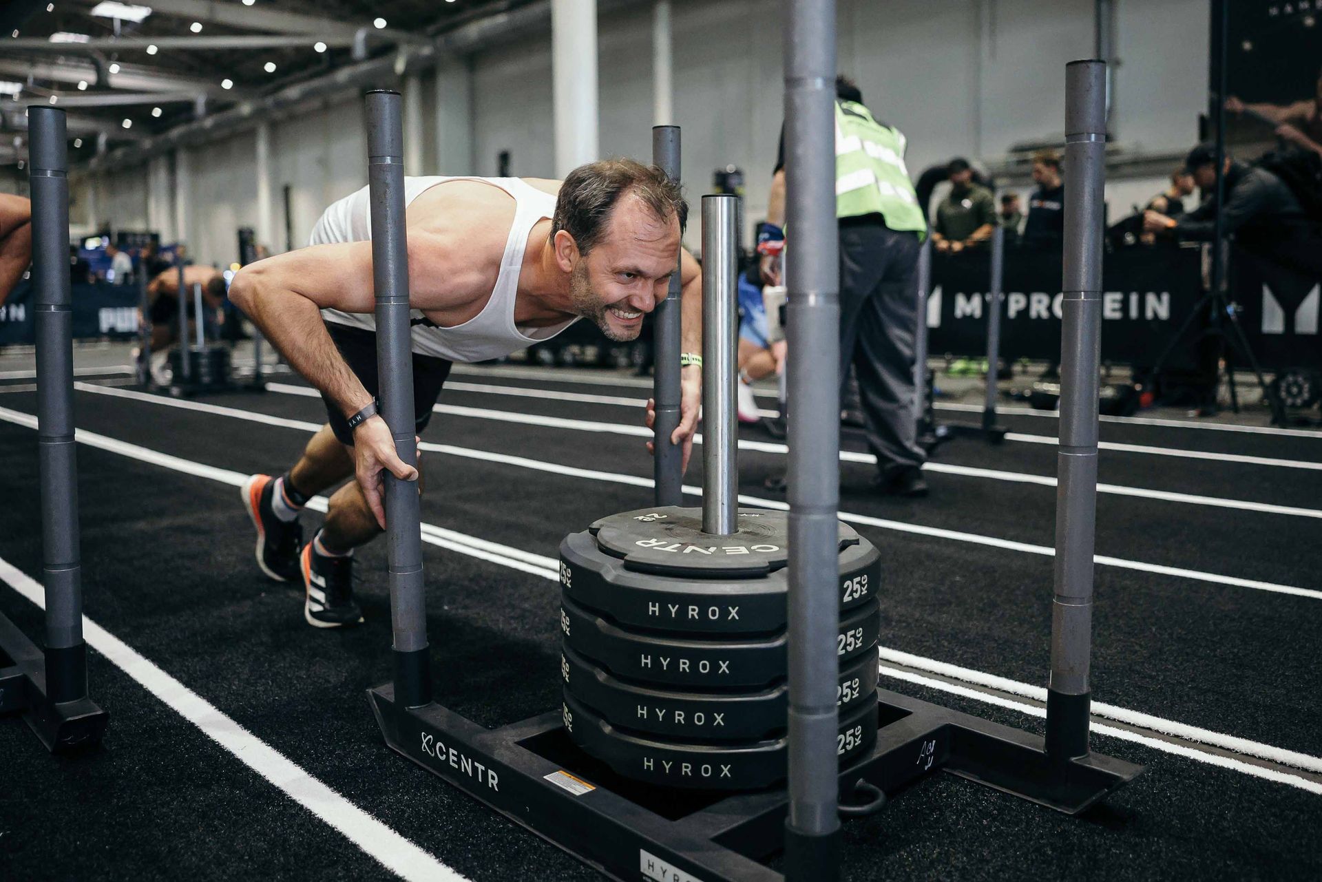 Mann im weißen Tanktop bei der HYROX Übung Sled Push
