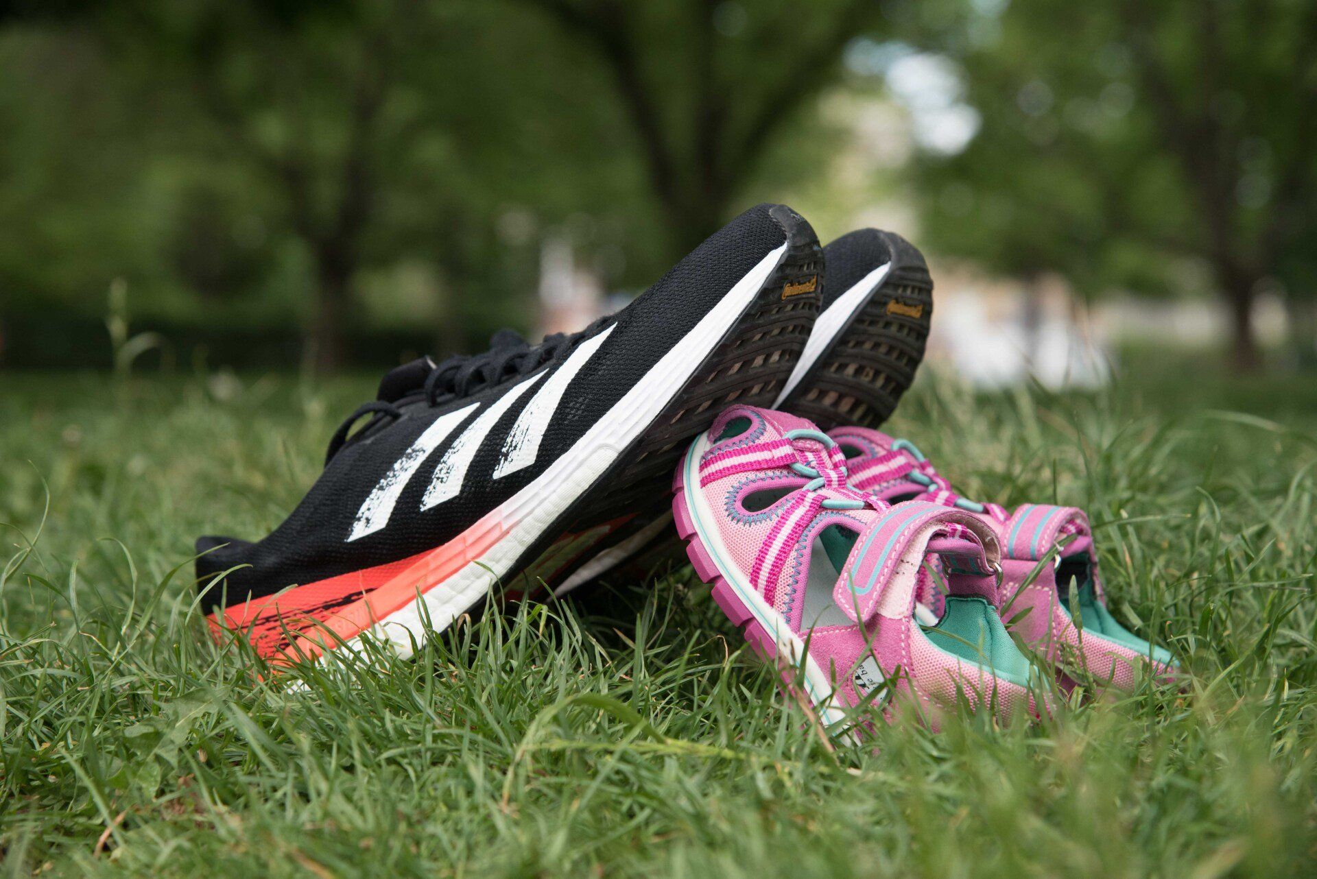 Sportschuhe eines Erwachsenen und Kindersandalen im Gras mit Bäumen