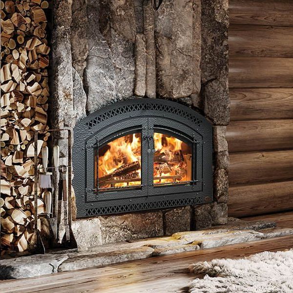 A fireplace in a log cabin with a pile of wood behind it.