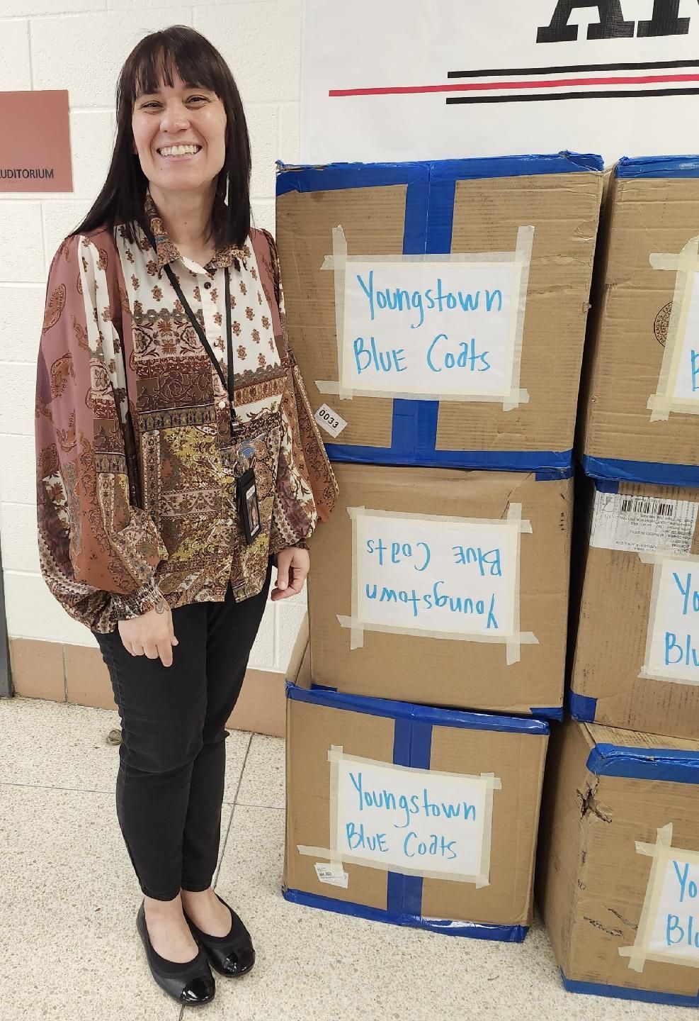 A woman is standing in front of a stack of cardboard boxes labeled blue coats