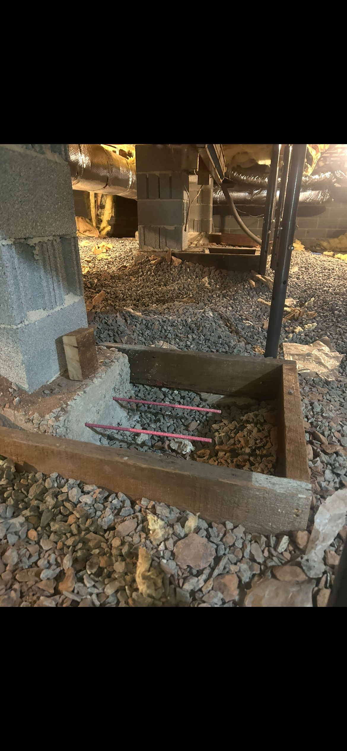Cinder block crawl space support pier resting on a concrete footer inside a wooden form surrounded by gravel.