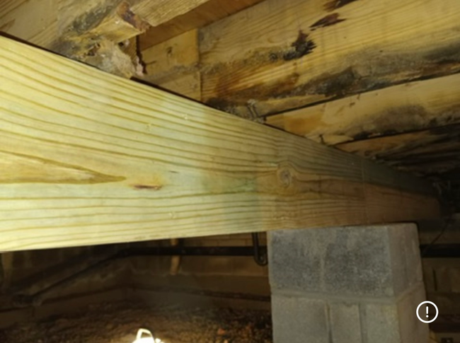 A new, light-colored wooden beam rests on a concrete block pier under a crawlspace with dark, weathered floor joists.