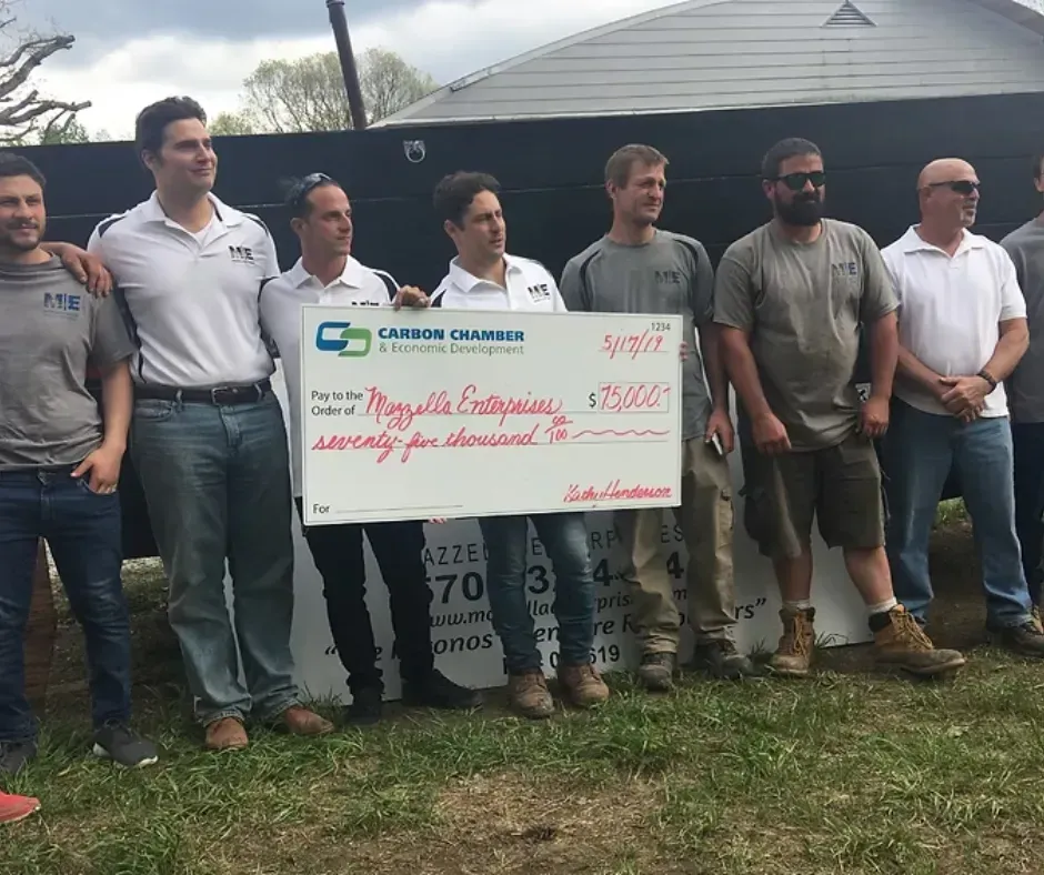 A group of people standing outdoors, holding a large check from Carbon Chamber & Economic Development for $70,000.