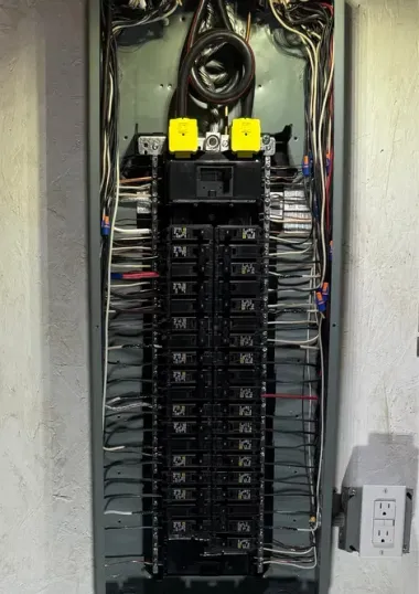 An open electrical panel featuring a central column of breakers, various wiring, and two yellow terminal blocks at the top.