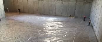A basement construction site with concrete walls, exposed pipes, and a plastic vapor barrier covering the floor.