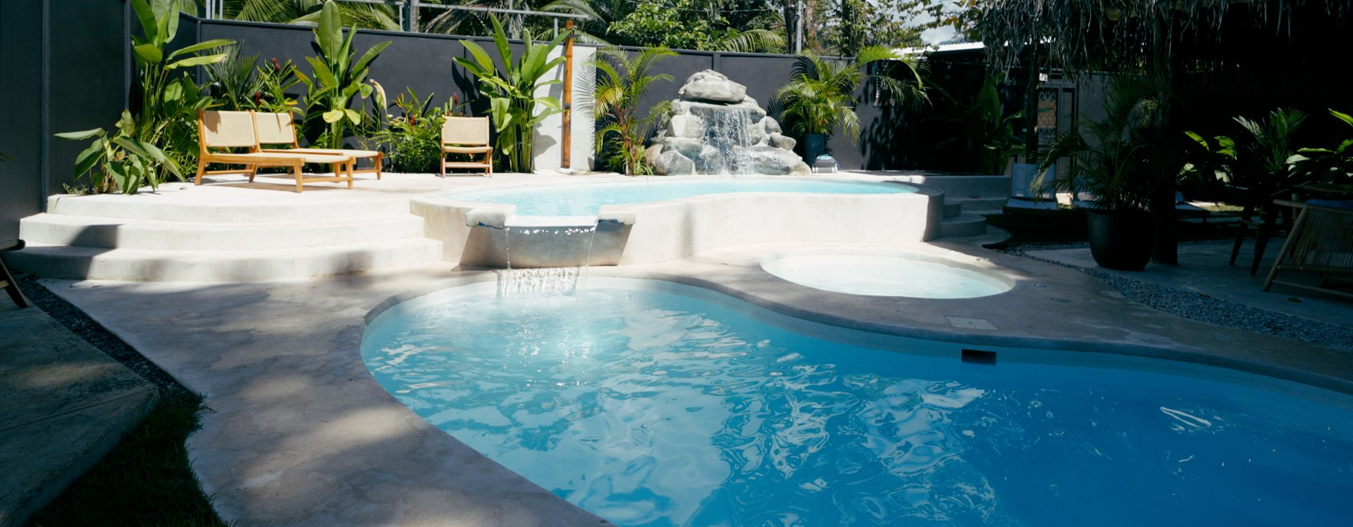 Technician adjusting pool pump equipment beside a backyard hot tub and swimming pool