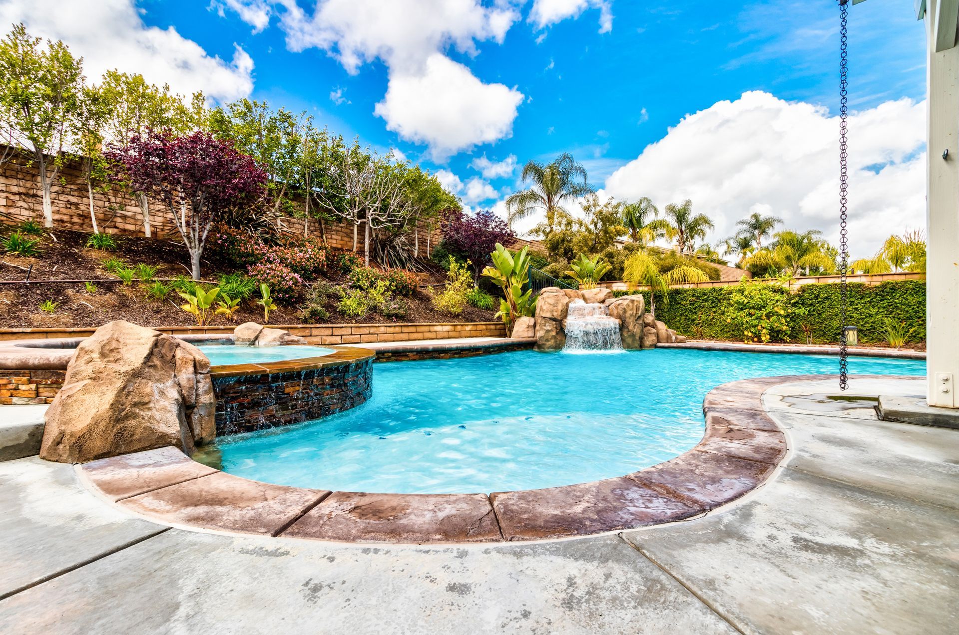 Person skimming a backyard swimming pool with a blue net on a sunny day