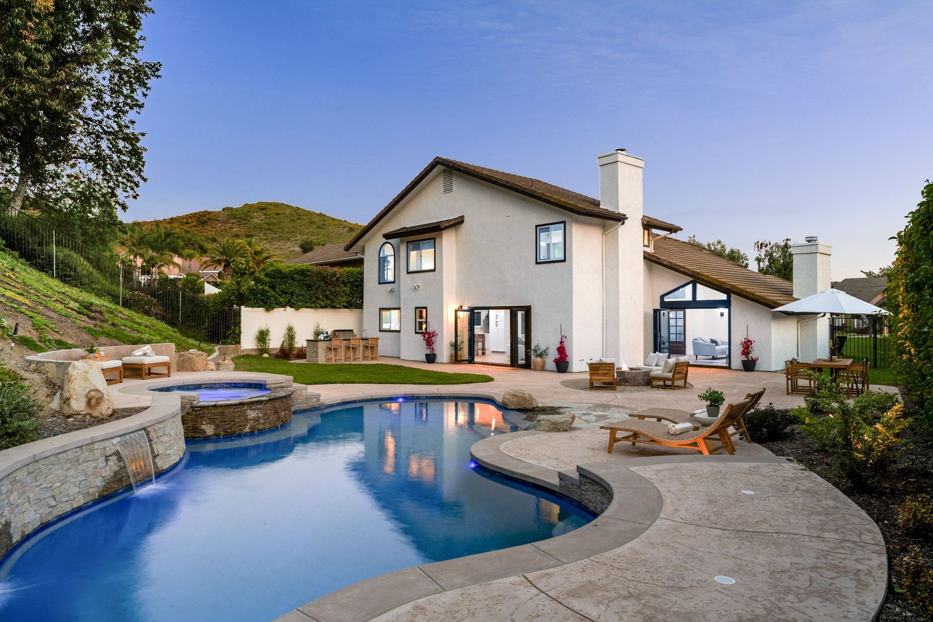Modern house with a curved backyard pool and stone patio at sunset