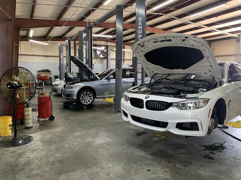 A white bmw is sitting on a lift in a garage with its hood open.
