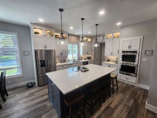 Modern kitchen with white cabinets, stainless appliances, and a large island under pendant lights.