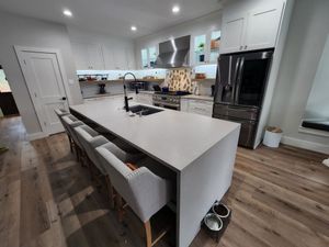 Bright modern kitchen with white island, stainless appliances, black stools, and wood floors