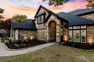 Brick house exterior with stone entry, dark roof, large windows, and sunset sky