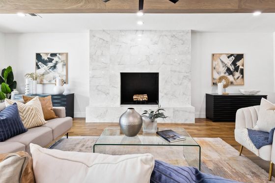Modern living room with marble fireplace, neutral sofas, glass coffee table, and abstract wall art.