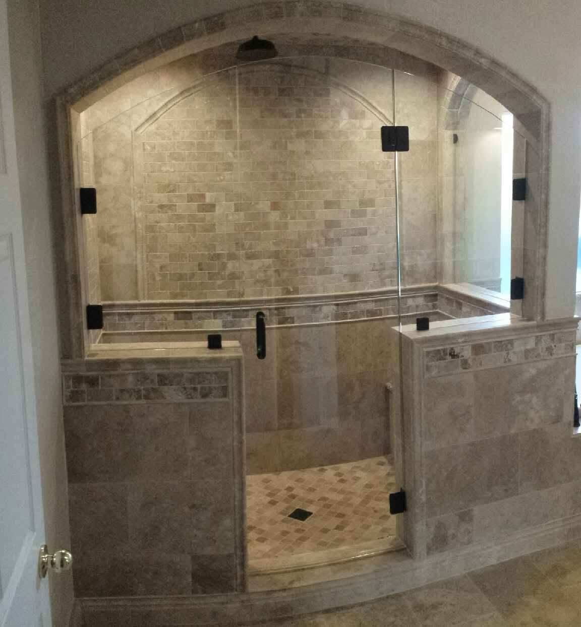 Walk-in tiled shower with glass door and arched stone alcove inside a bathroom