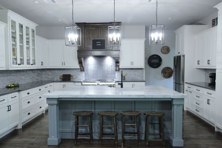 Modern white kitchen with a blue island, pendant lights, and stainless steel range hood