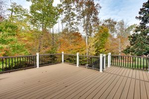 Spacious wooden deck with black railings overlooking autumn trees and a grassy yard