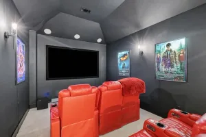 Modern home theater with red recliner seats, a large blank screen, and movie posters on dark walls