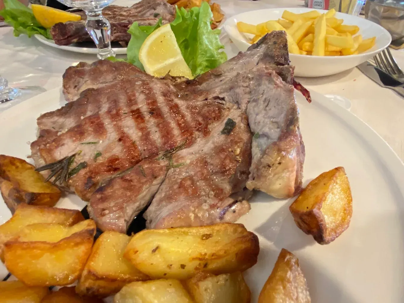 Costoletta di maiale alla griglia con patate arrosto, patatine fritte e fetta di limone su un piatto bianco.
