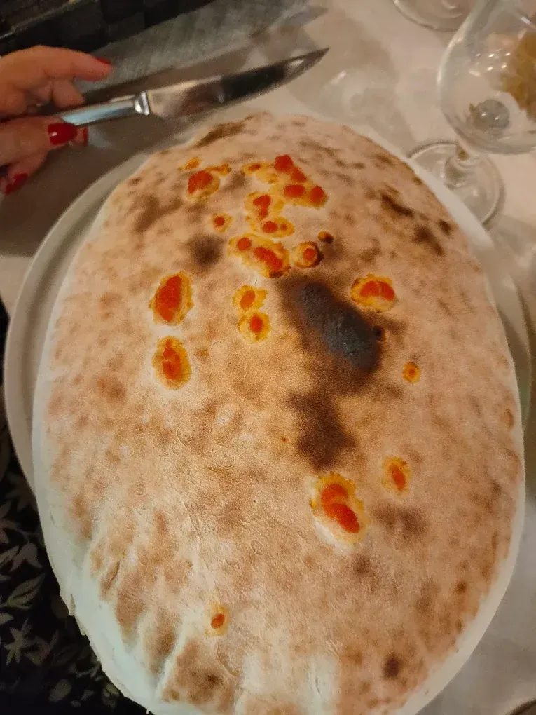 Pane grande, rotondo, cotto al forno, con salsa rossastra, tagliato a fette con un coltello.