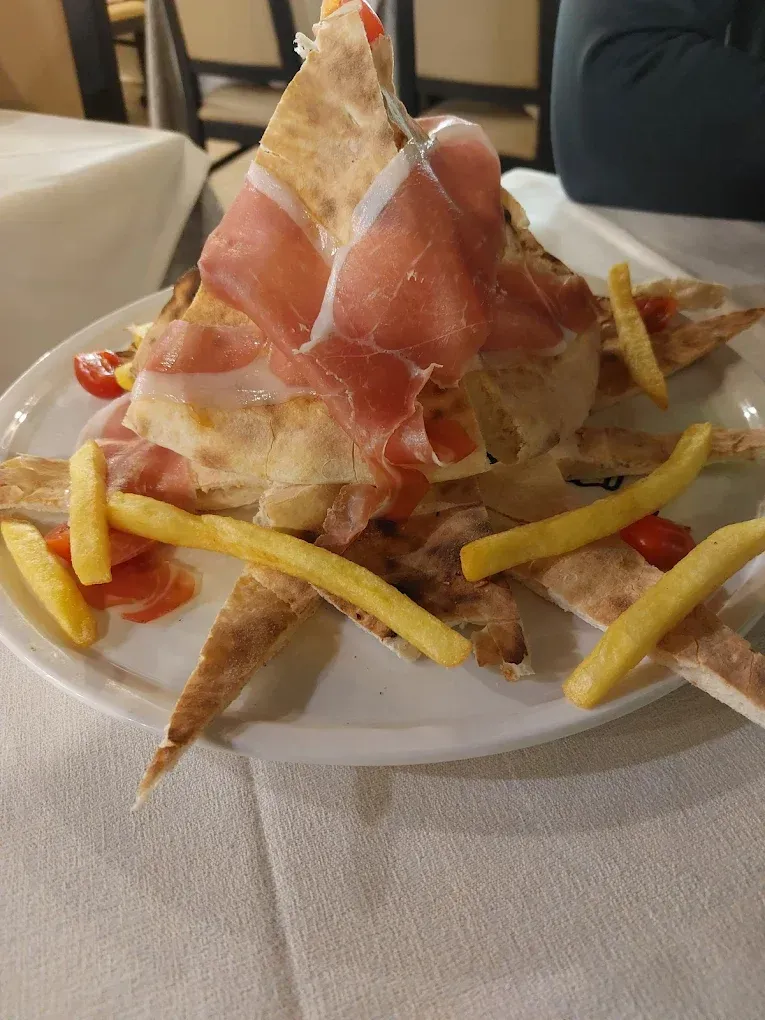 Piatto con pane, prosciutto, pomodori e patatine fritte disposti su un piatto bianco sopra una tovaglia.