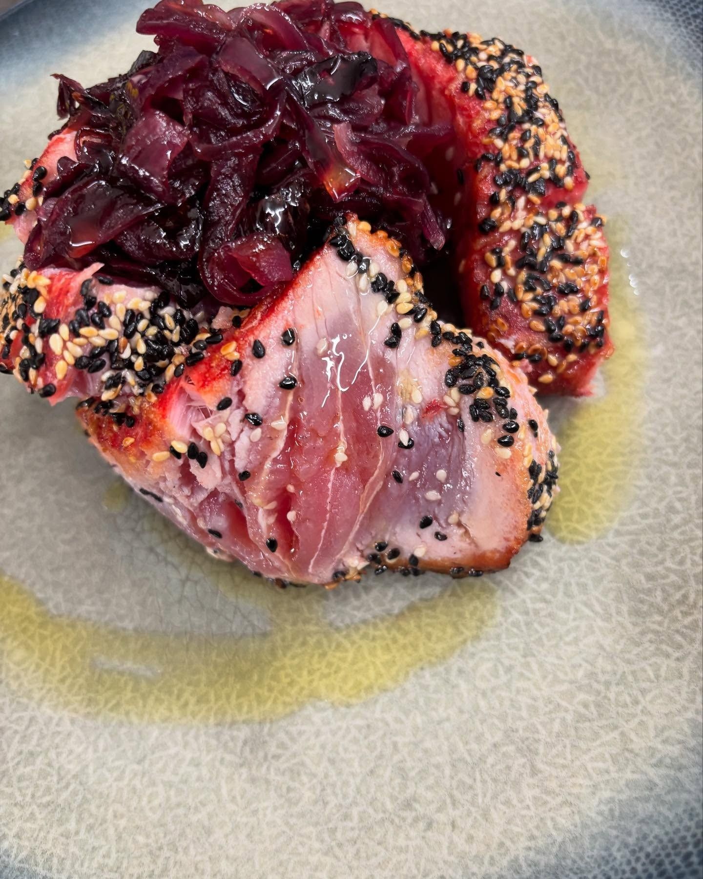 Tonno scottato con semi di sesamo e salsa di cipolle rosse, servito su un piatto grigio.