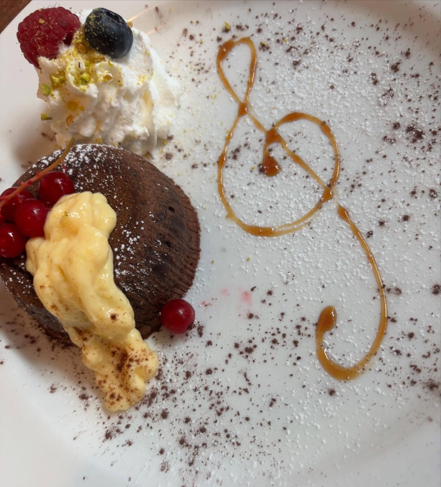 Torta al cioccolato fuso con chiave di violino al caramello, panna montata, frutti di bosco e spolverata di cacao in polvere.