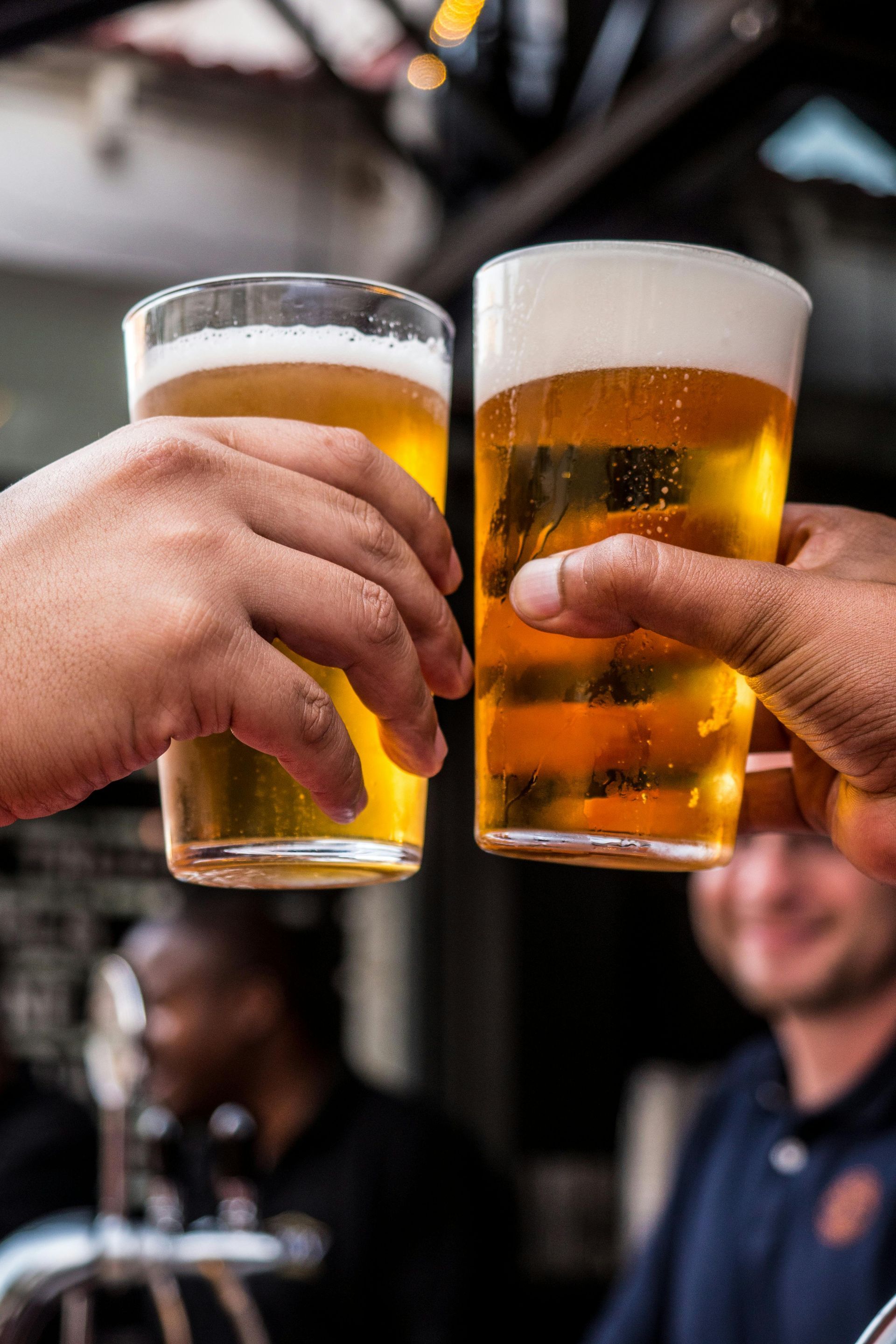 Due mani che brindano con bicchieri di birra, all'aperto.