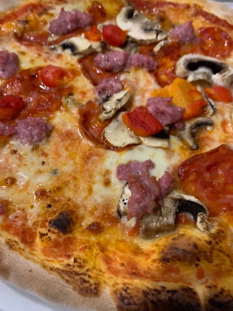 Primo piano di una pizza con salsiccia, funghi, peperoni rossi e pomodori su una crosta dorata.