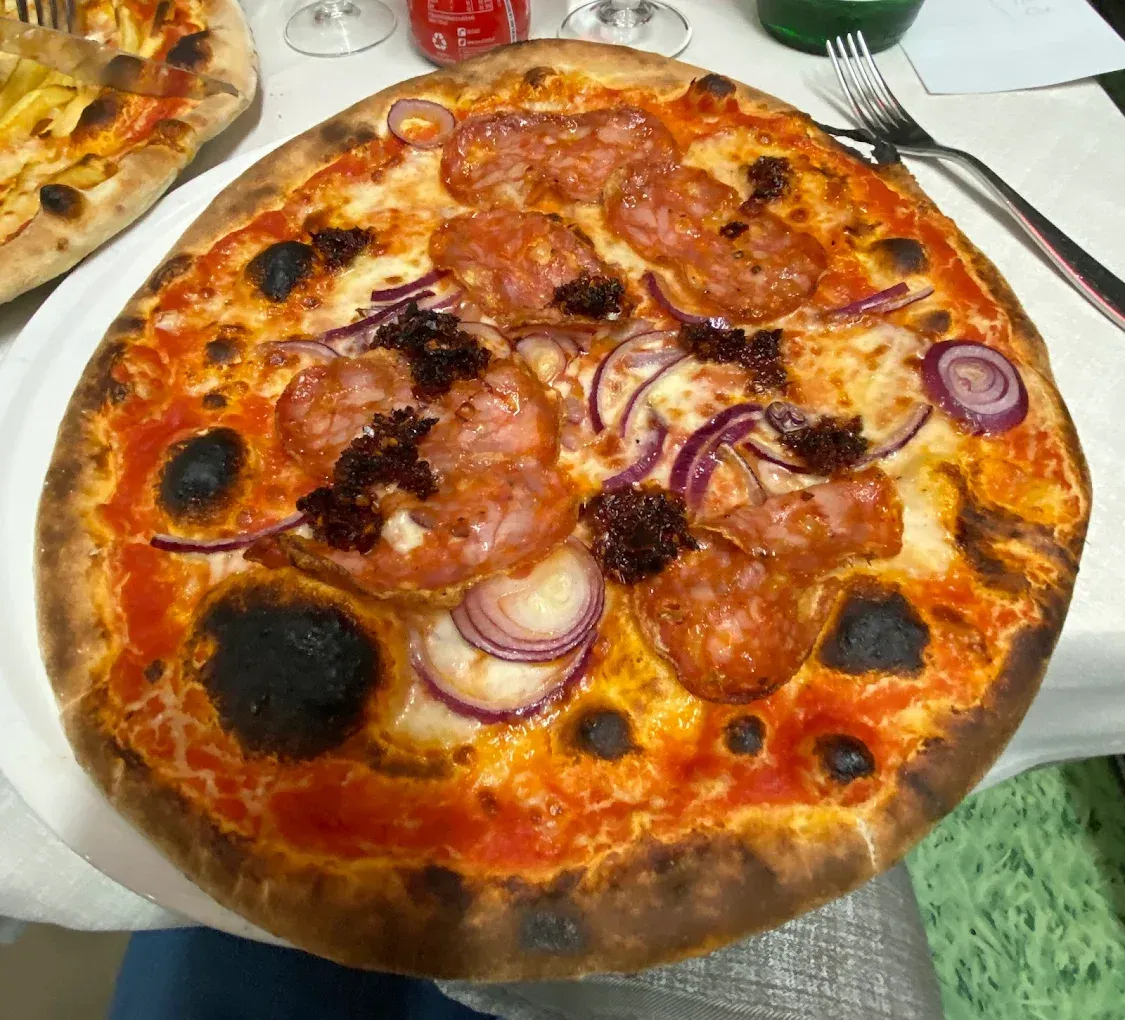 Pizza con pepperoni, cipolla rossa e macchie scure sulla crosta.