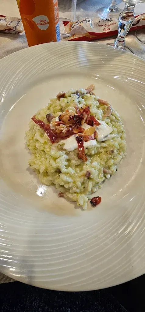 Risotto con pancetta e panna, servito su un piatto bianco. Sullo sfondo, un'aranciata e un bicchiere.