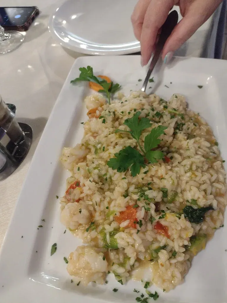 Risotto su un piatto bianco, guarnito con prezzemolo. Una mano con una forchetta infilata nel piatto.