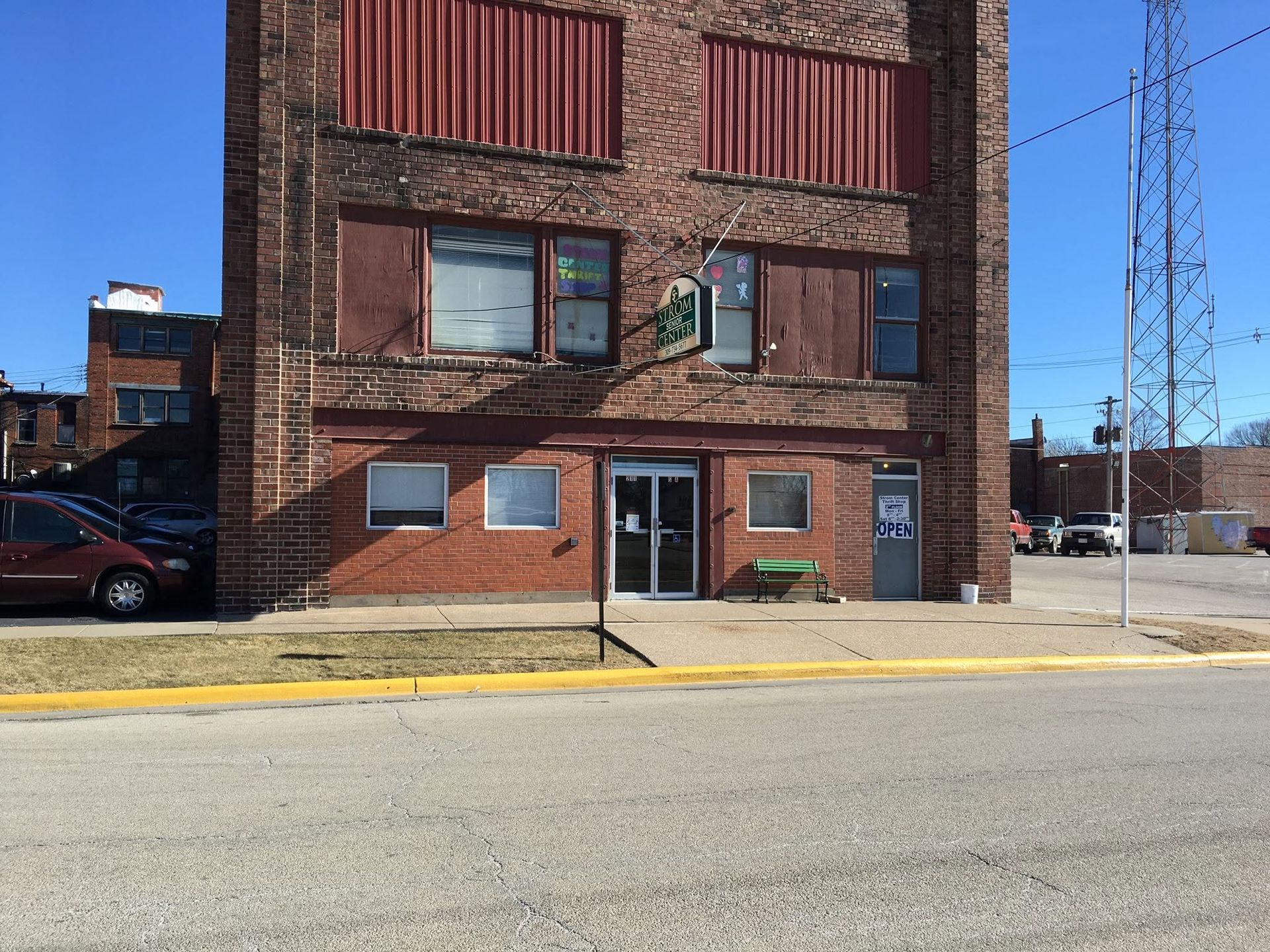 Brick building with red shutters and a dark entryway beside a street under a clear blue sky