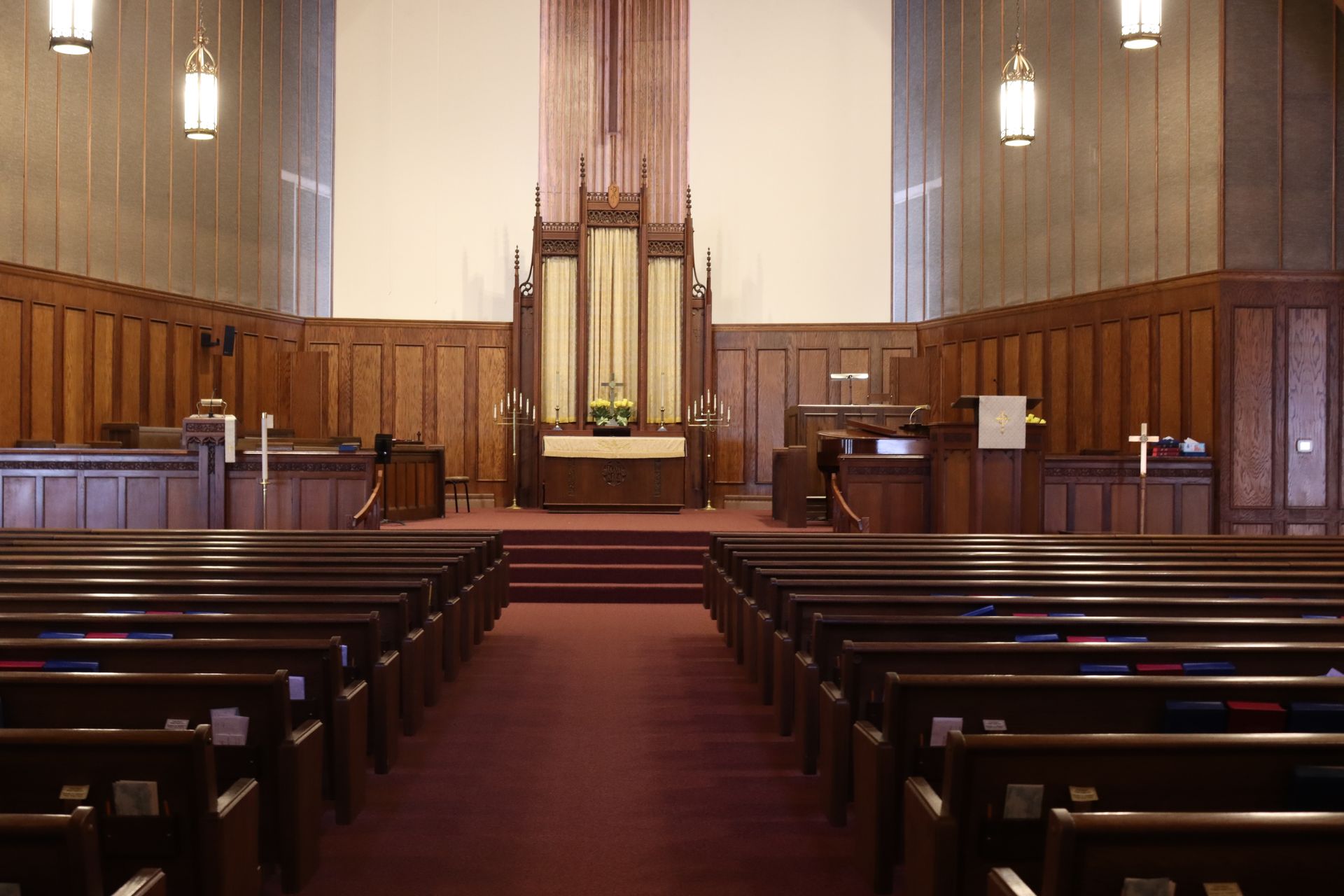 Empty church sanctuary with wooden pews, red carpet, and a central altar beneath tall organ pipes