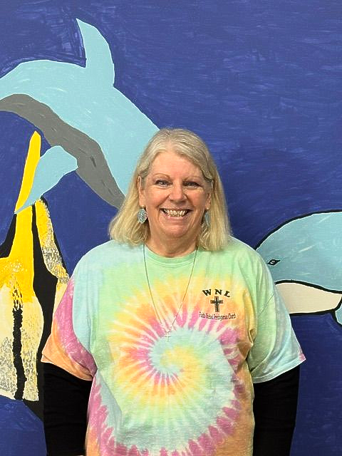Woman smiling in a rainbow tie-dye shirt standing before a dolphin mural