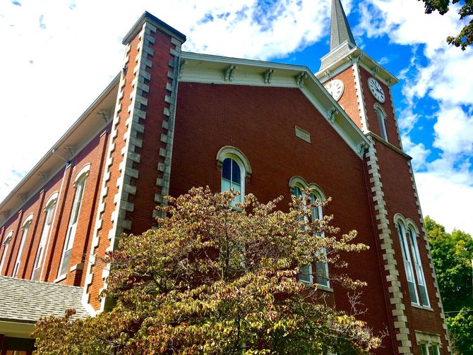 Red brick church with tall tower and white-trimmed windows against a blue sky