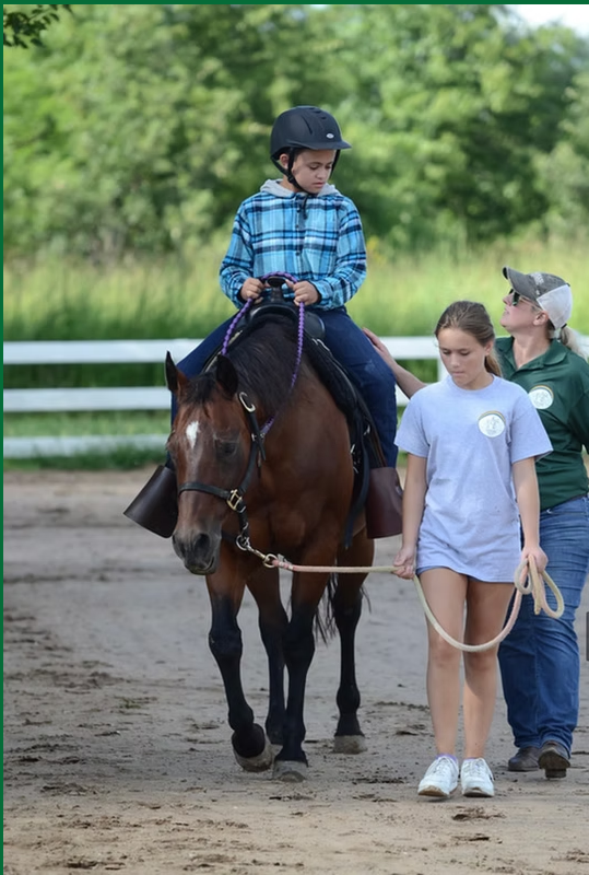 Child on horse with handler and trainer in an outdoor riding arena