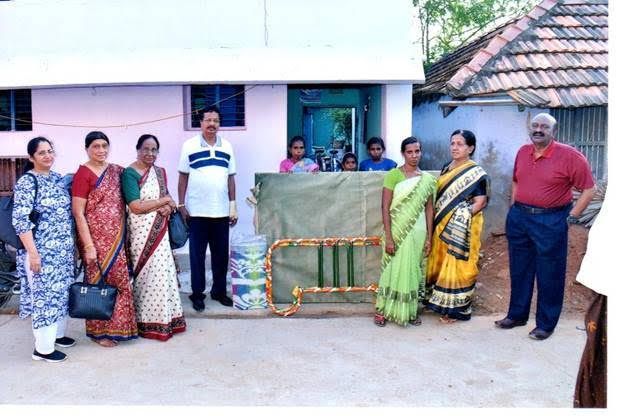 People standing outdoors beside a wrapped item and garlanded structure in front of a house