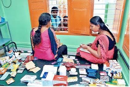 Two women sorting books and stationery on the floor in a bright room with a mirror and orange window frames