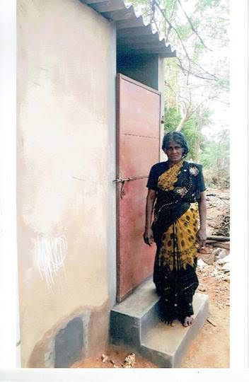 Woman in a black and yellow sari standing by a pink door at a small building entrance