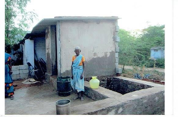 Person standing beside a small concrete house and water well in a rural yard