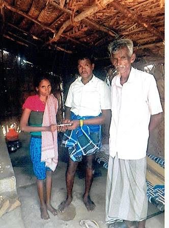 Three people standing inside a rustic hut, holding a small object together.