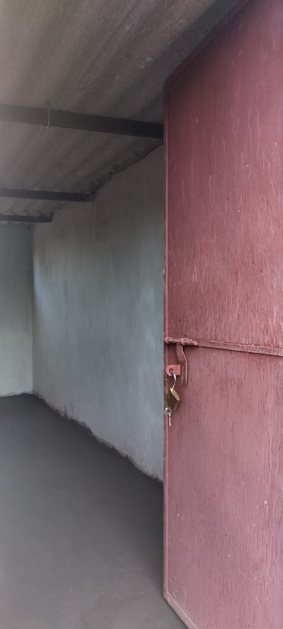 Red metal door partly open in a gray corridor with a corrugated roof